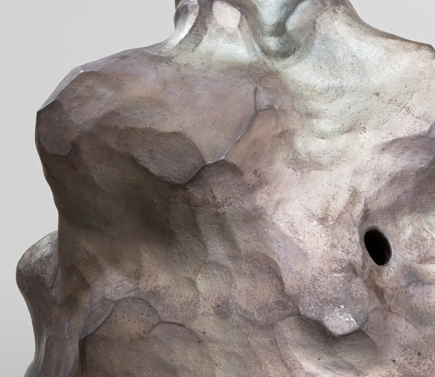 Die Skulptur hat organische Formen und erdige sowie metallische Farben. Sie läuft nach oben hin spitzer zu. Im oberen Teil befindet sich ein Loch. Detailansicht.