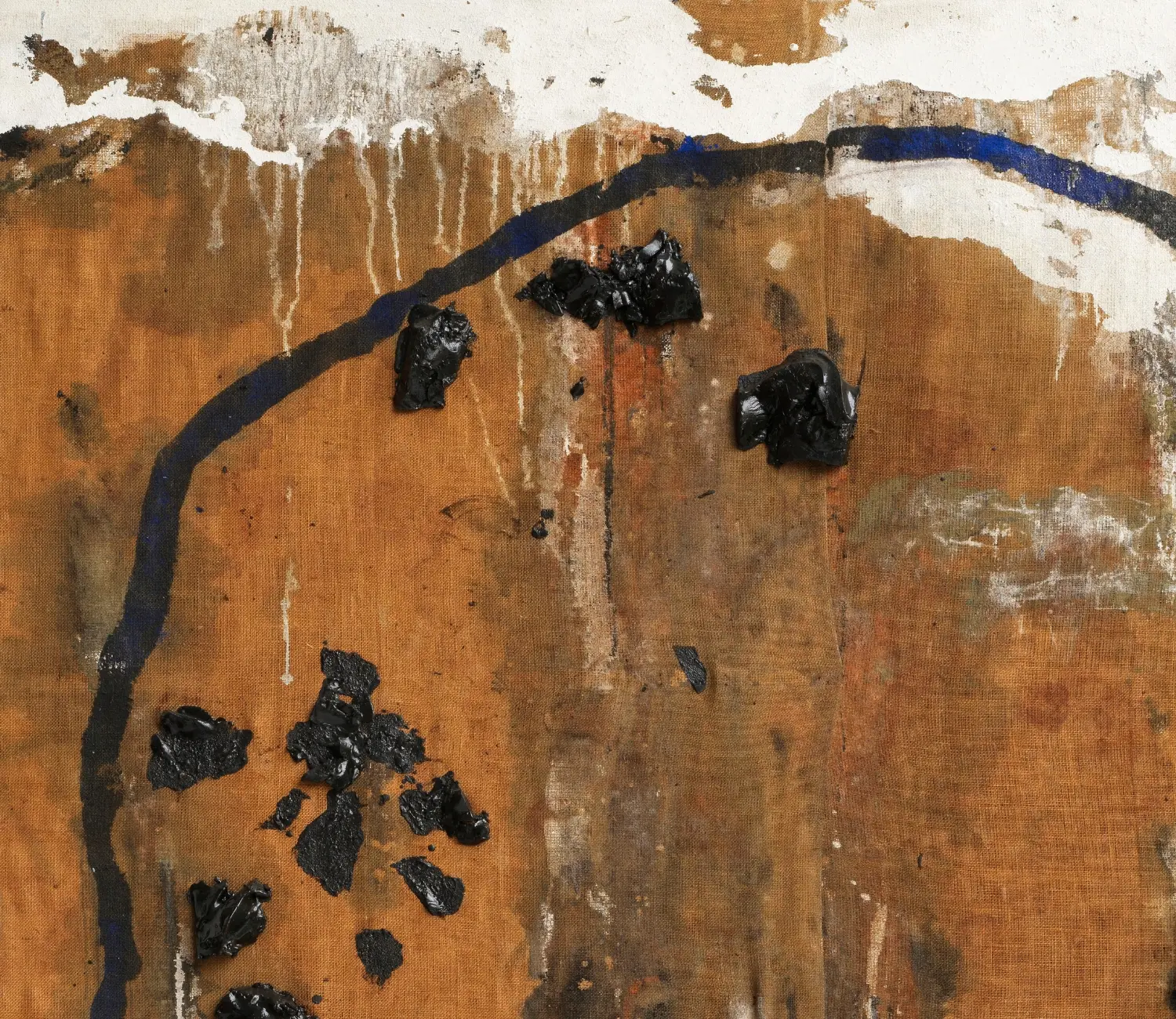 Abstraktes Gemälde von Emil Schumacher aus dem Jahr 1974 mit dem Titel »Indemini«. Die Komposition zeigt eine grob strukturierte, braune Fläche aus Rupfen, die von einer unregelmäßigen, schwarzen, bogenförmigen Linienführung umrahmt wird. Mehrere schwarze, reliefartige Farbflecken aus Asphalt sind auf der Leinwand verteilt und heben sich plastisch vom Hintergrund ab. Weiße Farbschichten sowie vereinzelte blaue Akzente ergänzen die Oberfläche. Die Malweise wirkt spontan und expressiv, die Materialien und Texturen sind deutlich sichtbar. Detailansicht.