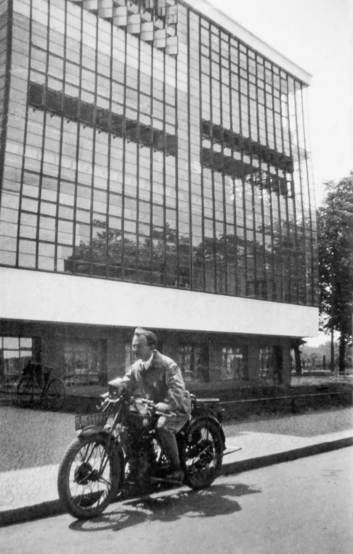 Heinrich Brocksieper sitzt auf einem Motorrad vor dem Bauhaus-Gebäude in Dessau, schwarz-weiß Fotografie