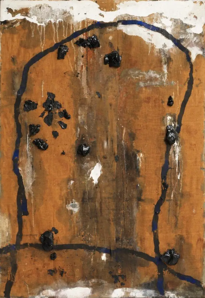 Abstraktes Gemälde von Emil Schumacher aus dem Jahr 1974 mit dem Titel »Indemini«. Die Komposition zeigt eine grob strukturierte, braune Fläche aus Rupfen, die von einer unregelmäßigen, schwarzen, bogenförmigen Linienführung umrahmt wird. Mehrere schwarze, reliefartige Farbflecken aus Asphalt sind auf der Leinwand verteilt und heben sich plastisch vom Hintergrund ab. Weiße Farbschichten sowie vereinzelte blaue Akzente ergänzen die Oberfläche. Die Malweise wirkt spontan und expressiv, die Materialien und Texturen sind deutlich sichtbar.